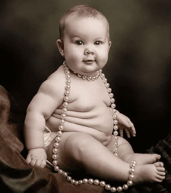 младенец 8 месяцев с явными признаками ожирения, сидит голенький с жемчужными бусами на шее