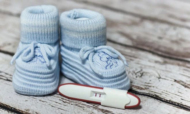 голубые пинетки рядом с которыми лежит положительный тест на беременность