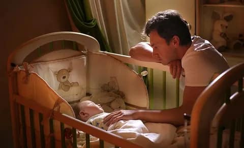 отец укладывает грудничка спать в кроватке