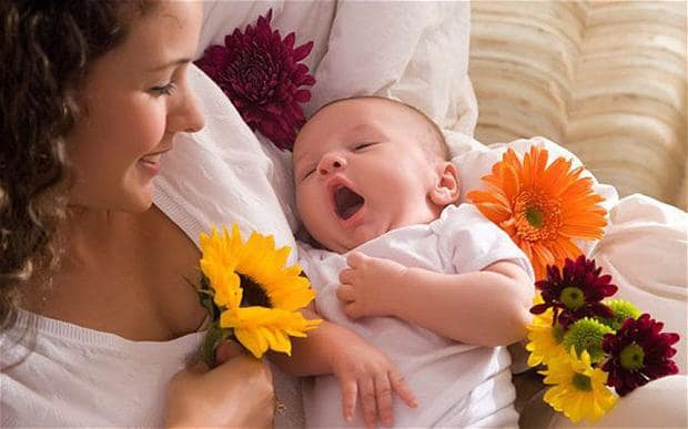 мать держит на руках зевающего младенца