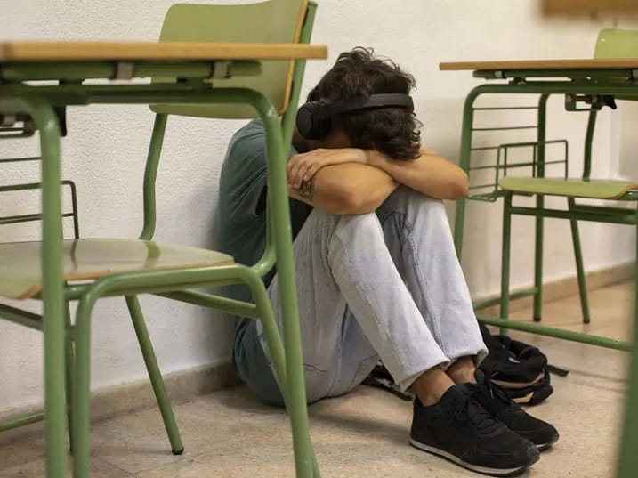 Мальчик, отвергнутый одноклассниками одиноко сидит между партами. Плачет, опустив голову на руки