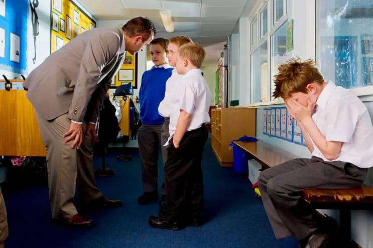 мальчик на скамейке плачет, с его обидчиками разговаривает учитель