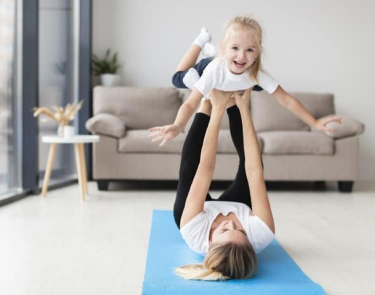 мать лежит на полу и на вытянутых руках и ногах держит девочку - упражнение "самолетик"