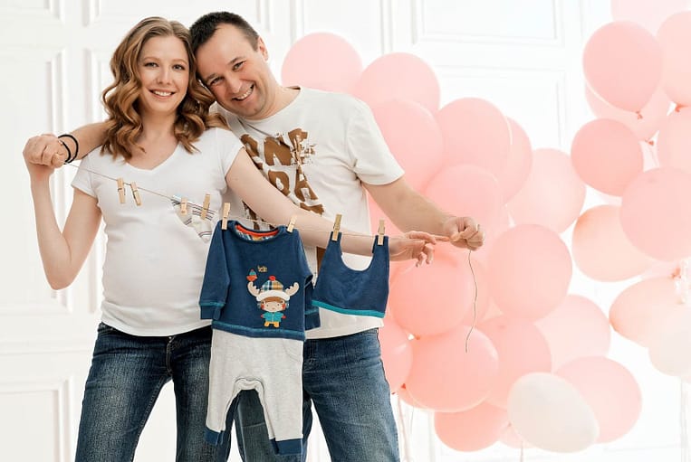 фото беременной с мужем, детской одеждой и воздушными шариками