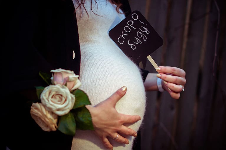 беременная держит в руках табличку "Скоро буду!"