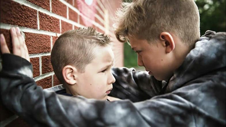 подросток прижал к стенке руками маленького мальчика и угрожает ему, мальчик напуган