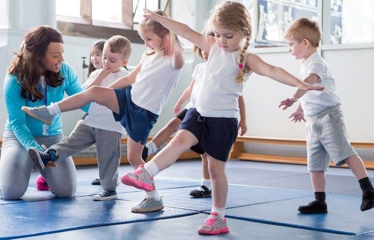 дошкольники занимаются гимнастикой в спортивной школе, тренер помогает им делать движения