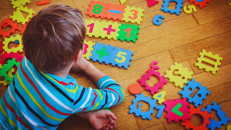 первоклассник лежит на полу в своей комнате и собирает математические примеры из пазлов