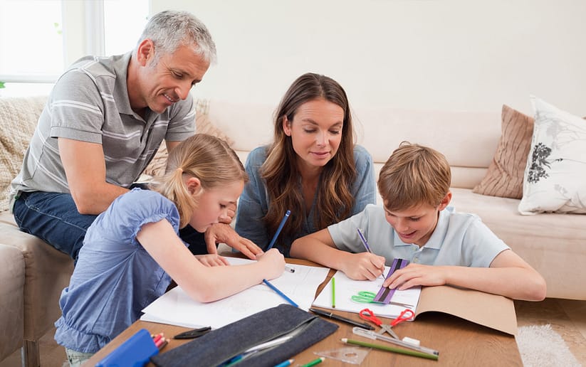 родители помогают детям развивать математические способности. Мальчик чертит линию с помощью линейки в тетради, девочка рисует карандашом