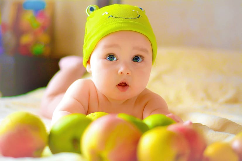 rebenok-s-yablokami, грудничок лежит на животе с опорой на предплечья, на нем зеленая шапочка, перед ним много яблок